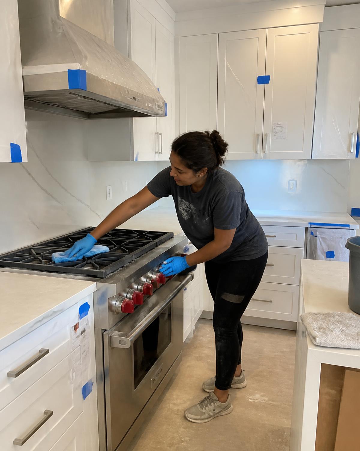 Cleaner wiping construction residue from a newly installed range and cabinetry after renovation